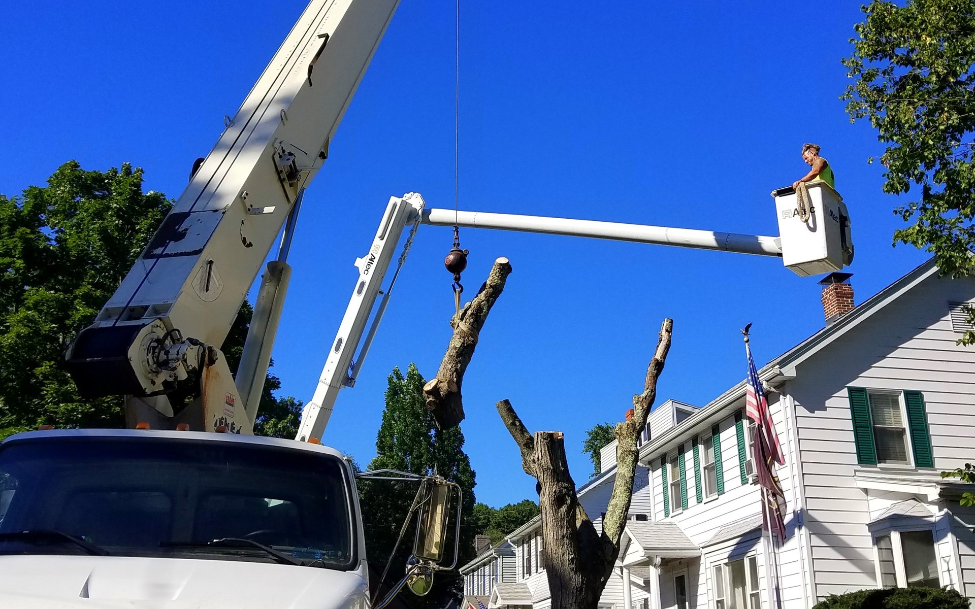 A crane and bucket truck removing a tree beside a house